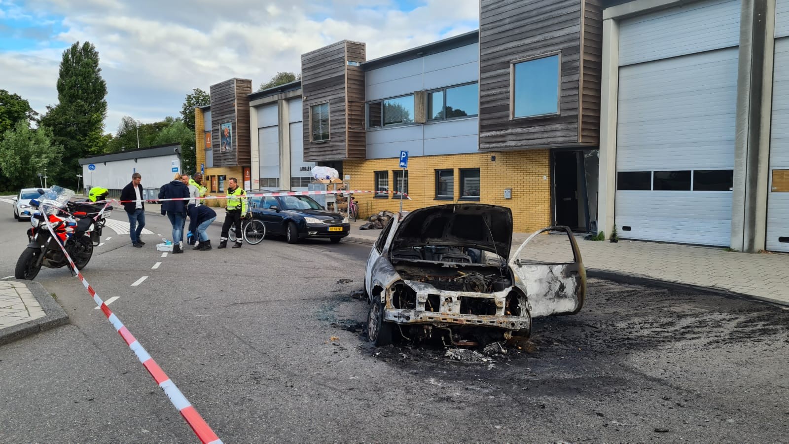 Een uitgebrande auto staat op de plek waar een ramkraak gepleegd is